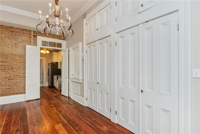 hall with a notable chandelier, baseboards, dark wood-style flooring, ornamental molding, and brick wall