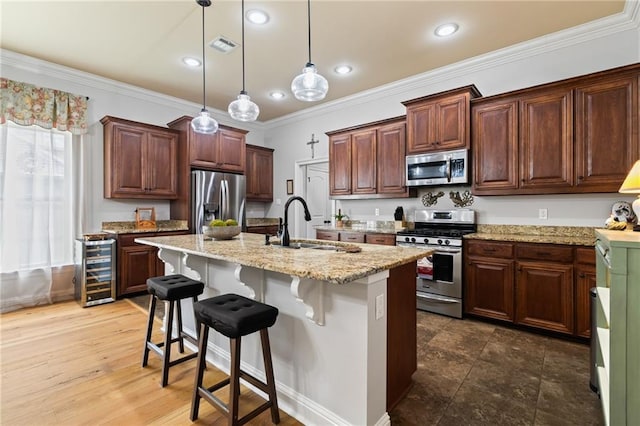 kitchen featuring crown molding, appliances with stainless steel finishes, decorative light fixtures, a kitchen bar, and an island with sink