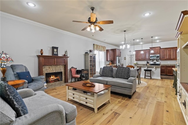 living room featuring ceiling fan with notable chandelier, ornamental molding, and light hardwood / wood-style flooring