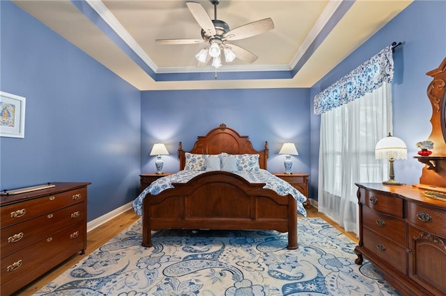 bedroom with ceiling fan, ornamental molding, light hardwood / wood-style flooring, and a tray ceiling