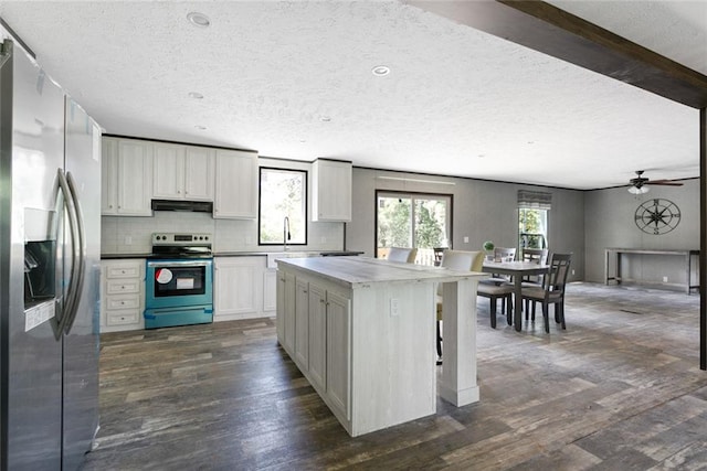 kitchen with white cabinets, dark hardwood / wood-style floors, a kitchen island, ceiling fan, and appliances with stainless steel finishes