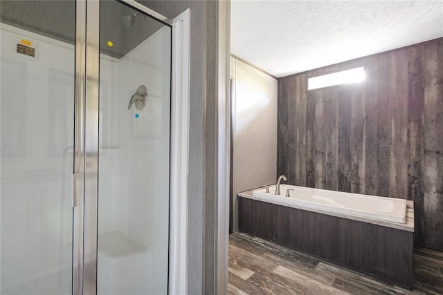 bathroom with hardwood / wood-style floors, wooden walls, a textured ceiling, and independent shower and bath