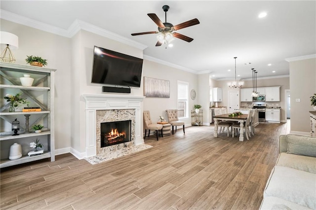 living room with a fireplace, light hardwood / wood-style floors, crown molding, and ceiling fan with notable chandelier