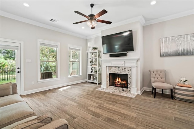 living room with ornamental molding, a premium fireplace, wood-type flooring, and ceiling fan