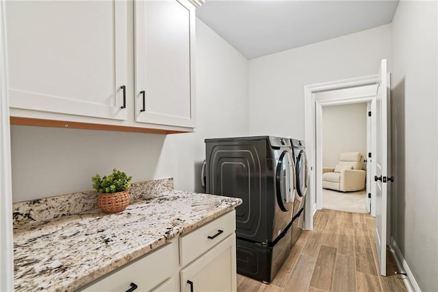 laundry area featuring cabinets, washing machine and dryer, and light hardwood / wood-style flooring