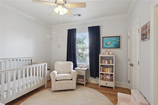 bedroom with light wood-type flooring, crown molding, ceiling fan, and a crib