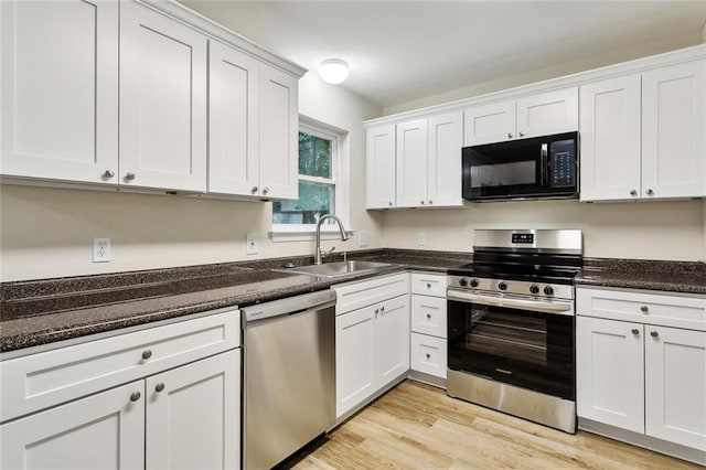 kitchen with dark stone counters, appliances with stainless steel finishes, sink, light hardwood / wood-style floors, and white cabinets