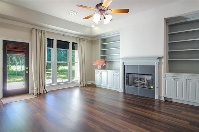 unfurnished living room with dark hardwood / wood-style flooring, ceiling fan, a tile fireplace, and built in features