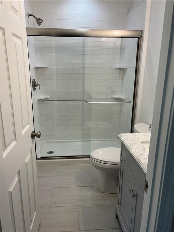 bathroom featuring a shower with door, vanity, and toilet