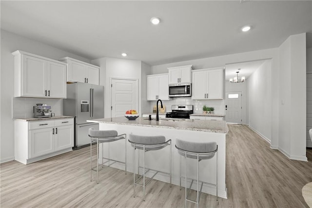 kitchen featuring light hardwood / wood-style flooring, tasteful backsplash, a kitchen island with sink, white cabinetry, and appliances with stainless steel finishes