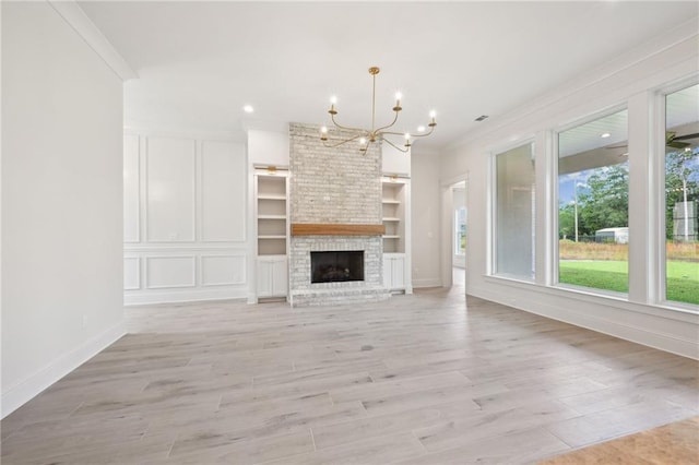 unfurnished living room with a brick fireplace, light hardwood / wood-style floors, an inviting chandelier, and ornamental molding