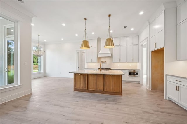 kitchen with pendant lighting, premium range hood, an island with sink, and white cabinets