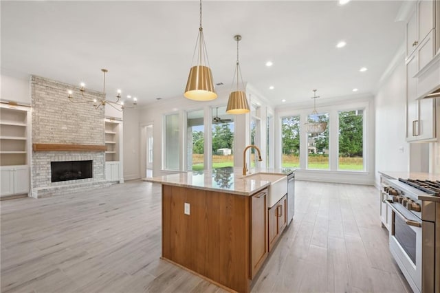 kitchen with stainless steel appliances, a fireplace, pendant lighting, light wood-type flooring, and a large island with sink