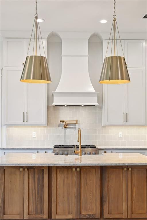 kitchen with white cabinetry, custom exhaust hood, a kitchen island with sink, pendant lighting, and decorative backsplash