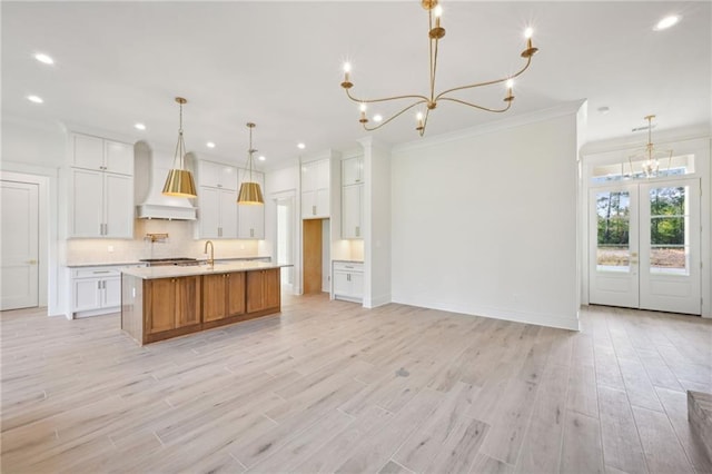 kitchen with a spacious island, custom range hood, white cabinetry, and light wood-type flooring