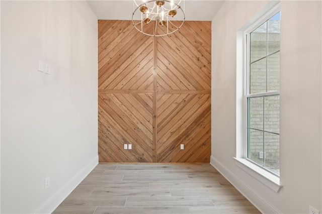 empty room featuring light hardwood / wood-style flooring, wooden walls, a healthy amount of sunlight, and a notable chandelier