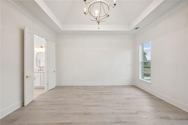 unfurnished room featuring an inviting chandelier, light hardwood / wood-style floors, and a raised ceiling