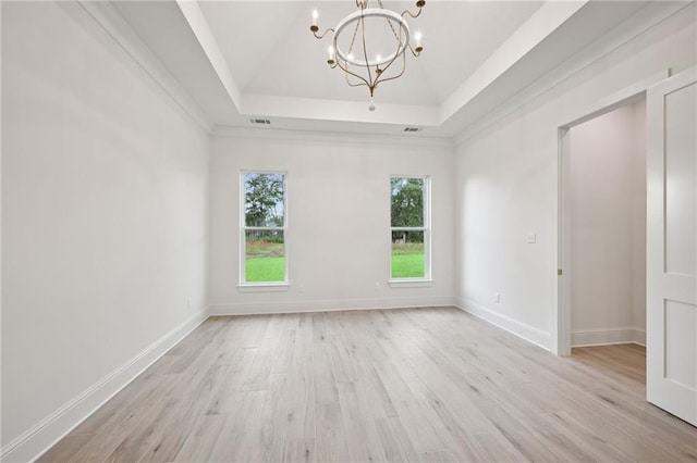 spare room with a chandelier, a raised ceiling, and light hardwood / wood-style flooring