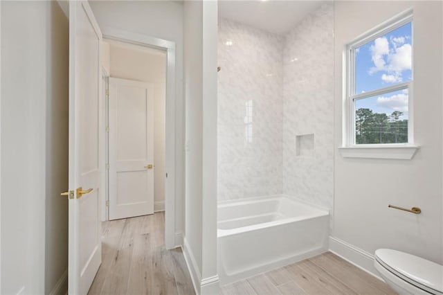 bathroom with wood-type flooring, toilet, and tiled shower / bath combo