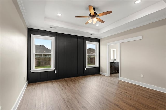 empty room with a tray ceiling, hardwood / wood-style flooring, ceiling fan, and crown molding