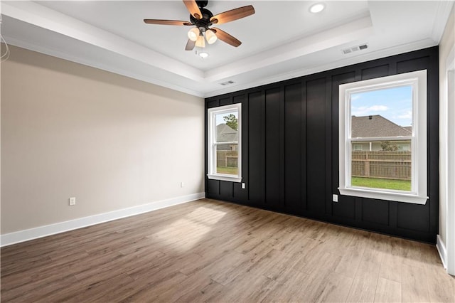 spare room with light hardwood / wood-style floors, ceiling fan, ornamental molding, and a tray ceiling