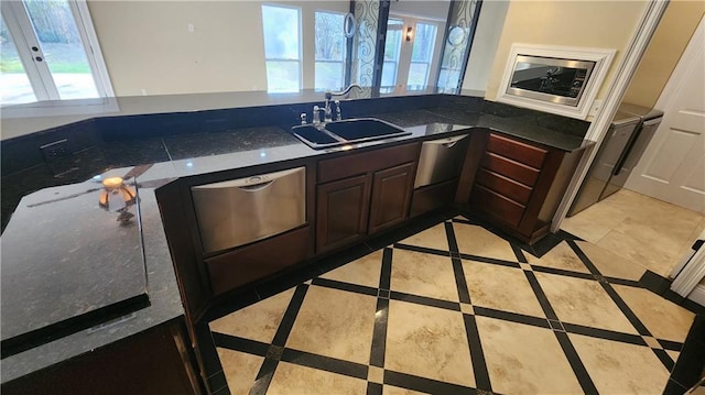 kitchen with dark brown cabinets, a wealth of natural light, dark stone counters, and sink