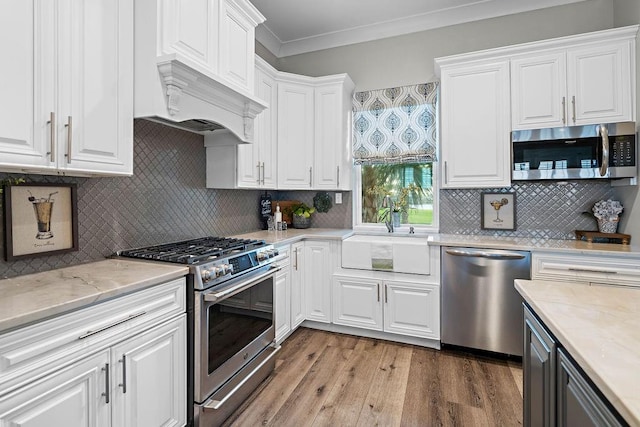 kitchen featuring stainless steel appliances, light hardwood / wood-style floors, white cabinetry, sink, and ornamental molding