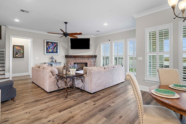 living room featuring a fireplace, hardwood / wood-style flooring, ceiling fan with notable chandelier, and ornamental molding