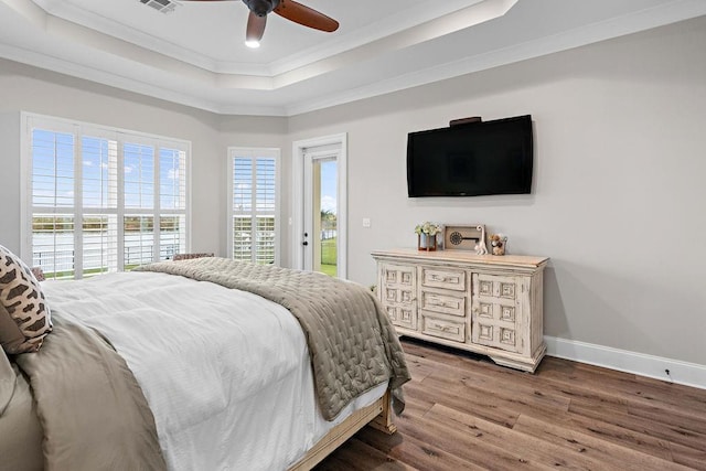 bedroom with ornamental molding, ceiling fan, wood-type flooring, a raised ceiling, and access to outside