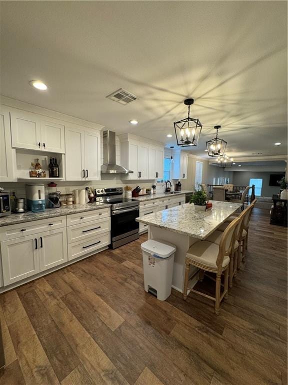 kitchen featuring white cabinetry, electric range, wall chimney range hood, pendant lighting, and a kitchen island