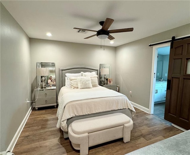 bedroom with a barn door, ceiling fan, ensuite bathroom, and dark wood-type flooring