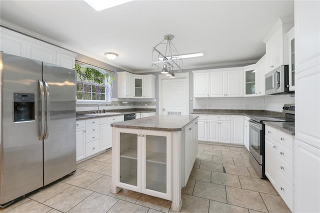 kitchen with appliances with stainless steel finishes, hanging light fixtures, decorative backsplash, white cabinets, and a center island