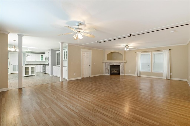 unfurnished living room featuring light hardwood / wood-style floors, a tiled fireplace, ceiling fan with notable chandelier, crown molding, and decorative columns