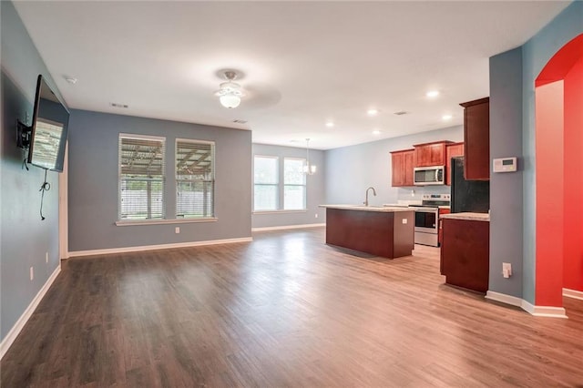 kitchen with appliances with stainless steel finishes, hanging light fixtures, hardwood / wood-style floors, ceiling fan, and a kitchen island with sink