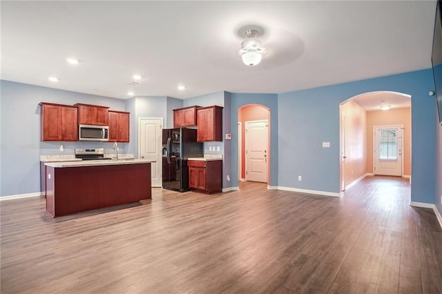 kitchen featuring a center island with sink, stainless steel appliances, hardwood / wood-style flooring, and ceiling fan