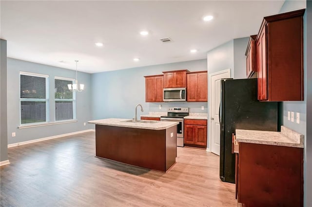 kitchen with appliances with stainless steel finishes, hanging light fixtures, sink, light hardwood / wood-style floors, and a kitchen island with sink