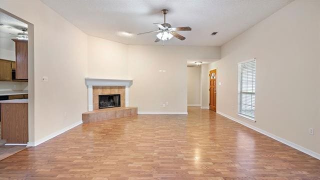 unfurnished living room featuring ceiling fan, light hardwood / wood-style flooring, and a tiled fireplace