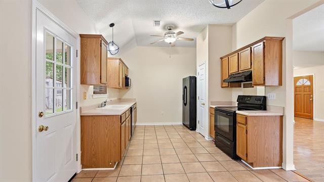 kitchen with vaulted ceiling, black appliances, light tile patterned floors, ceiling fan, and pendant lighting