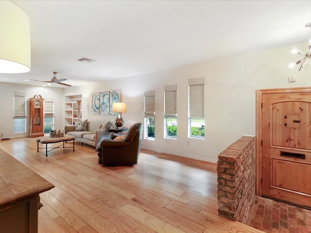 living room featuring ceiling fan with notable chandelier and light hardwood / wood-style flooring