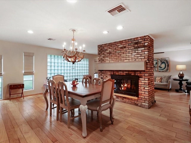 dining space with a fireplace, light hardwood / wood-style flooring, and a chandelier