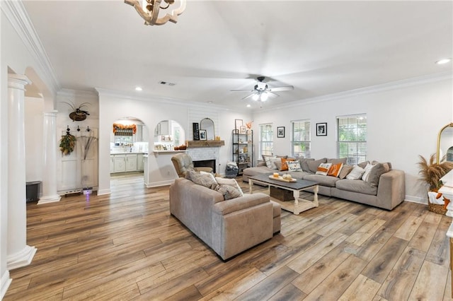 living room featuring ornamental molding, ornate columns, a large fireplace, light hardwood / wood-style floors, and ceiling fan