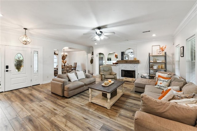 living room with wood-type flooring, a stone fireplace, ceiling fan with notable chandelier, and ornamental molding