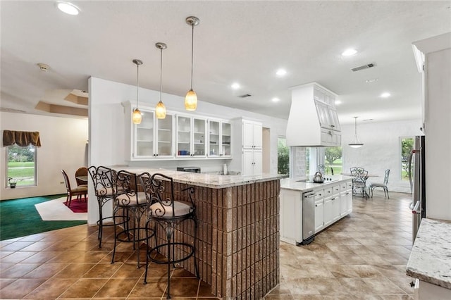 kitchen featuring light stone counters, white cabinetry, pendant lighting, and a healthy amount of sunlight