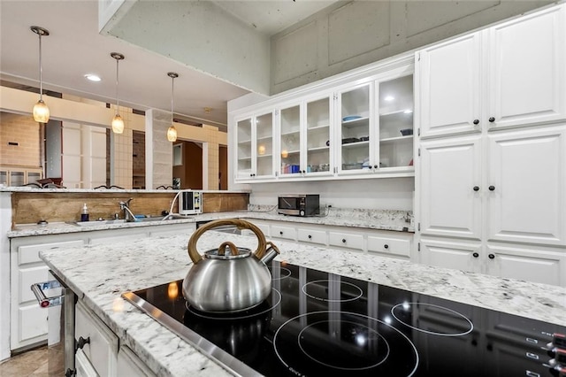 kitchen with decorative light fixtures, light stone countertops, sink, white cabinets, and black electric cooktop