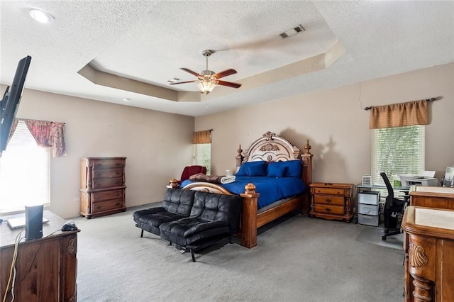 bedroom featuring a textured ceiling, light carpet, ceiling fan, and a raised ceiling