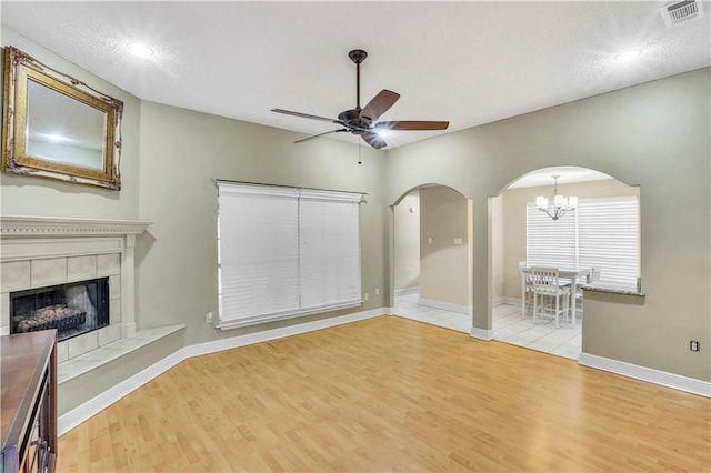 unfurnished living room with ceiling fan with notable chandelier, light hardwood / wood-style flooring, and a tile fireplace