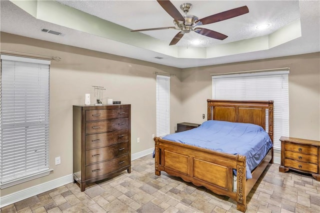 bedroom with a textured ceiling, ceiling fan, and a tray ceiling