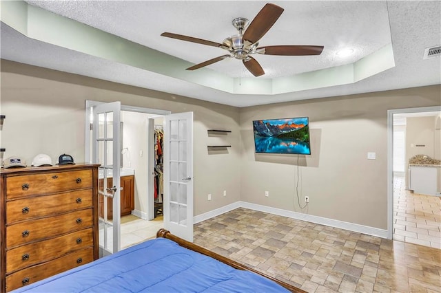 bedroom featuring ceiling fan, a textured ceiling, a spacious closet, a tray ceiling, and connected bathroom