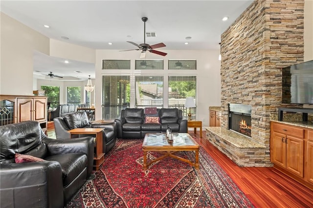 living room featuring ceiling fan, a stone fireplace, and dark hardwood / wood-style flooring