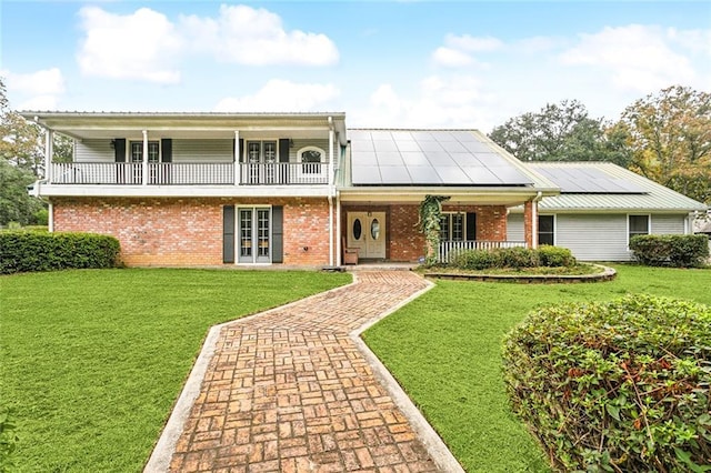 front facade with a balcony, a front lawn, brick siding, a porch, and solar panels